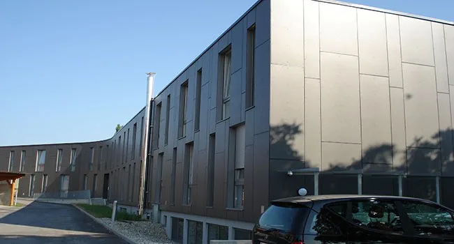 Mehrgeschossiges Gebäude mit grauer Plattenfassade, Straßenseite