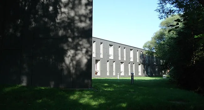 Blick zwischen zwei Gebäuden auf einen Wohnbau mit Fensterreihe und Wiese